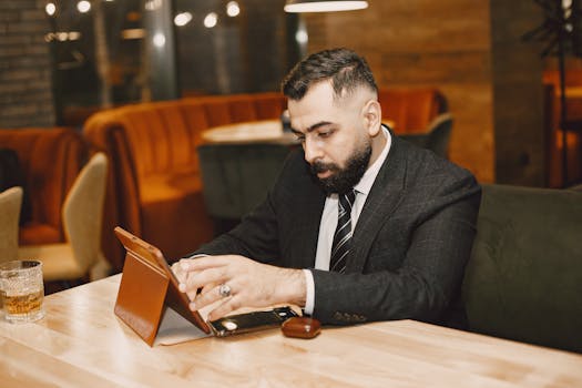 A professional adult male in a suit using a tablet in a stylish indoor cafe setting.