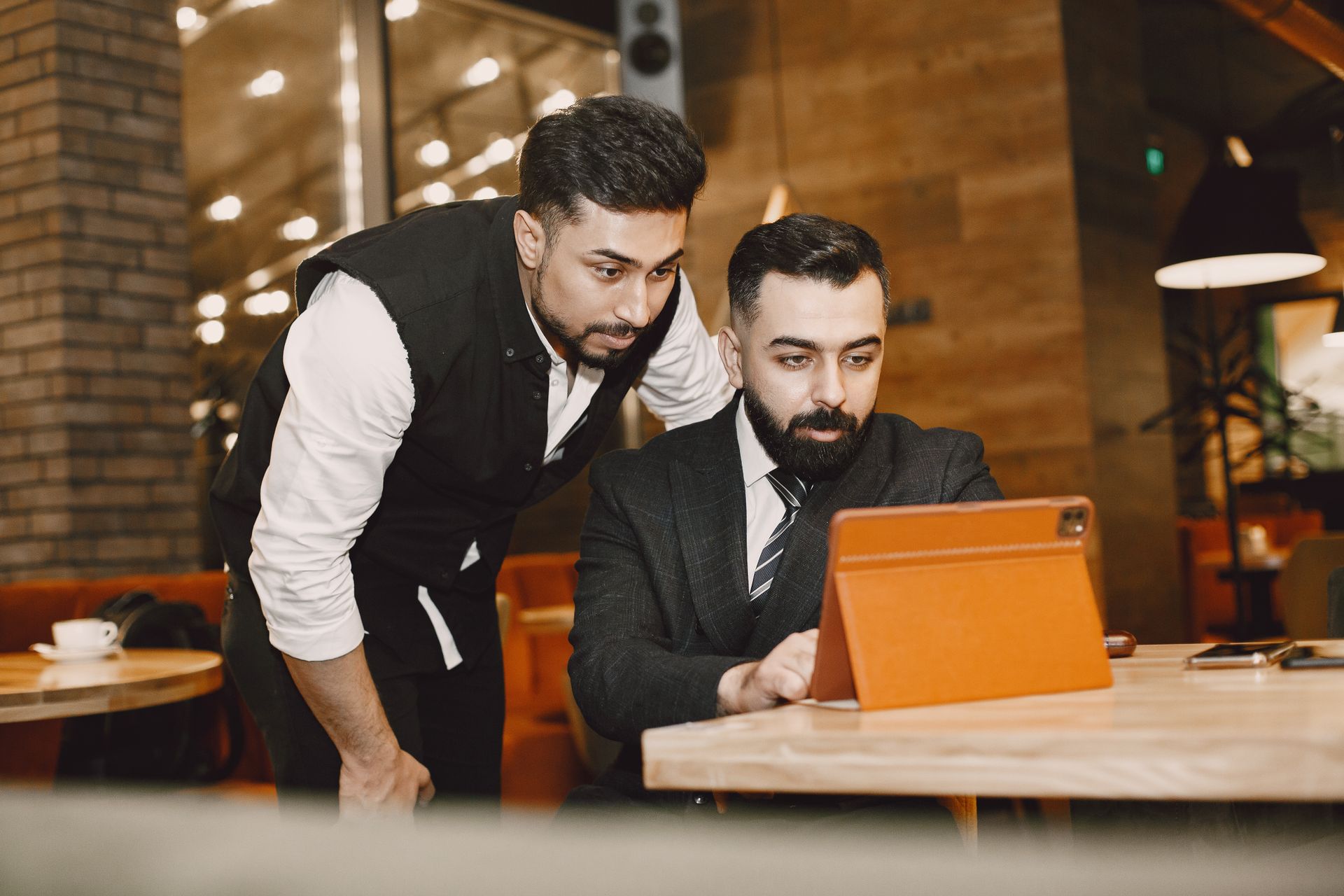 Two businessmen using a tablet in a modern restaurant setting, collaborating on a project.
