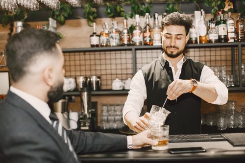 Free A bartender stirs a cocktail while serving a customer at a trendy bar setting. Stock Photo