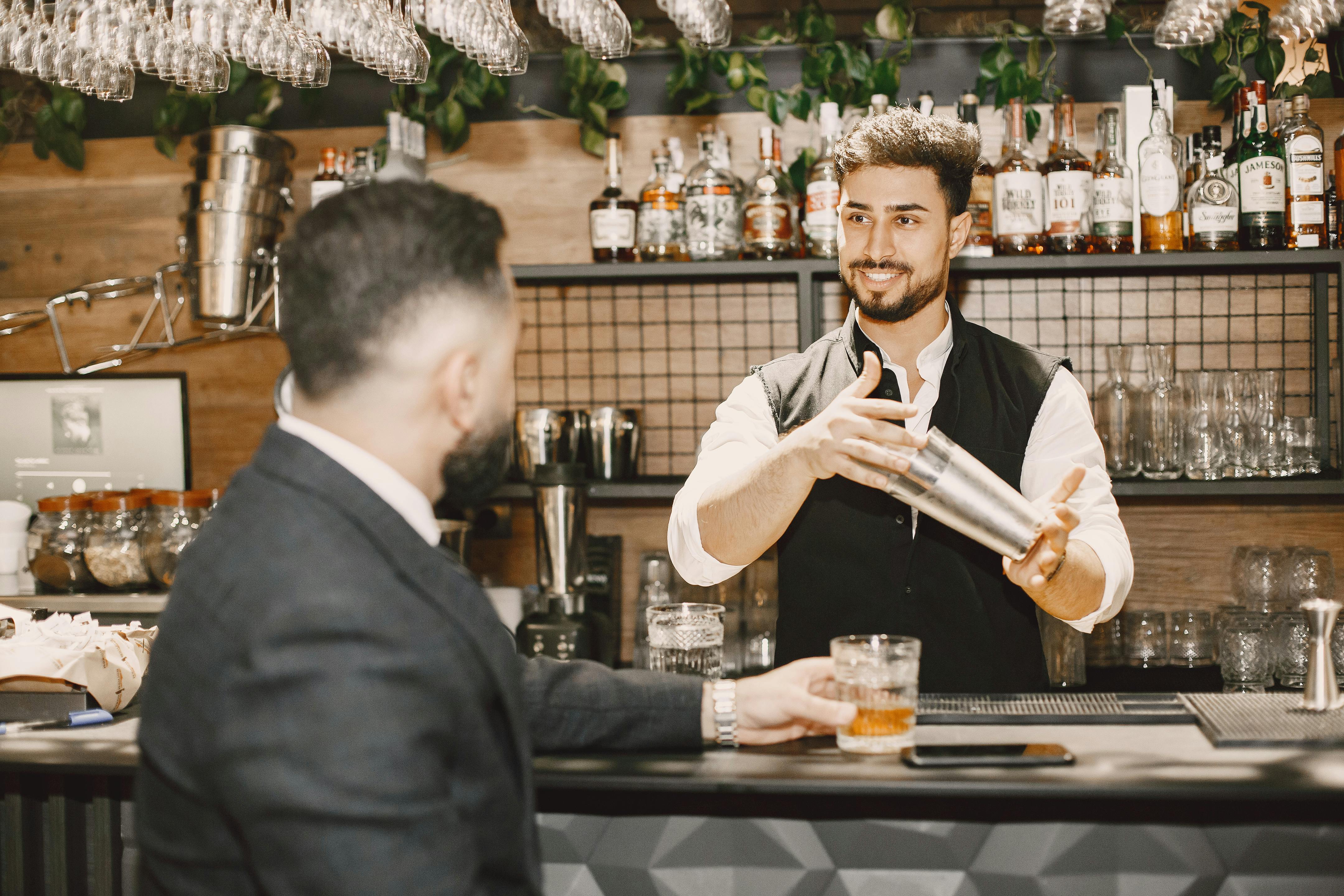 A guest having a positive interaction with a well-dressed bartender using professional bar tools - hospitality staff uniforms
