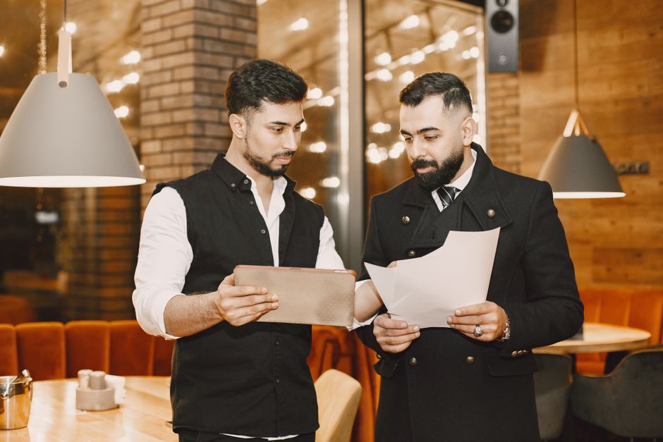Two businessmen reviewing documents and a tablet in a modern indoor setting. Two businessmen reviewing documents and a tablet in a modern indoor setting.
