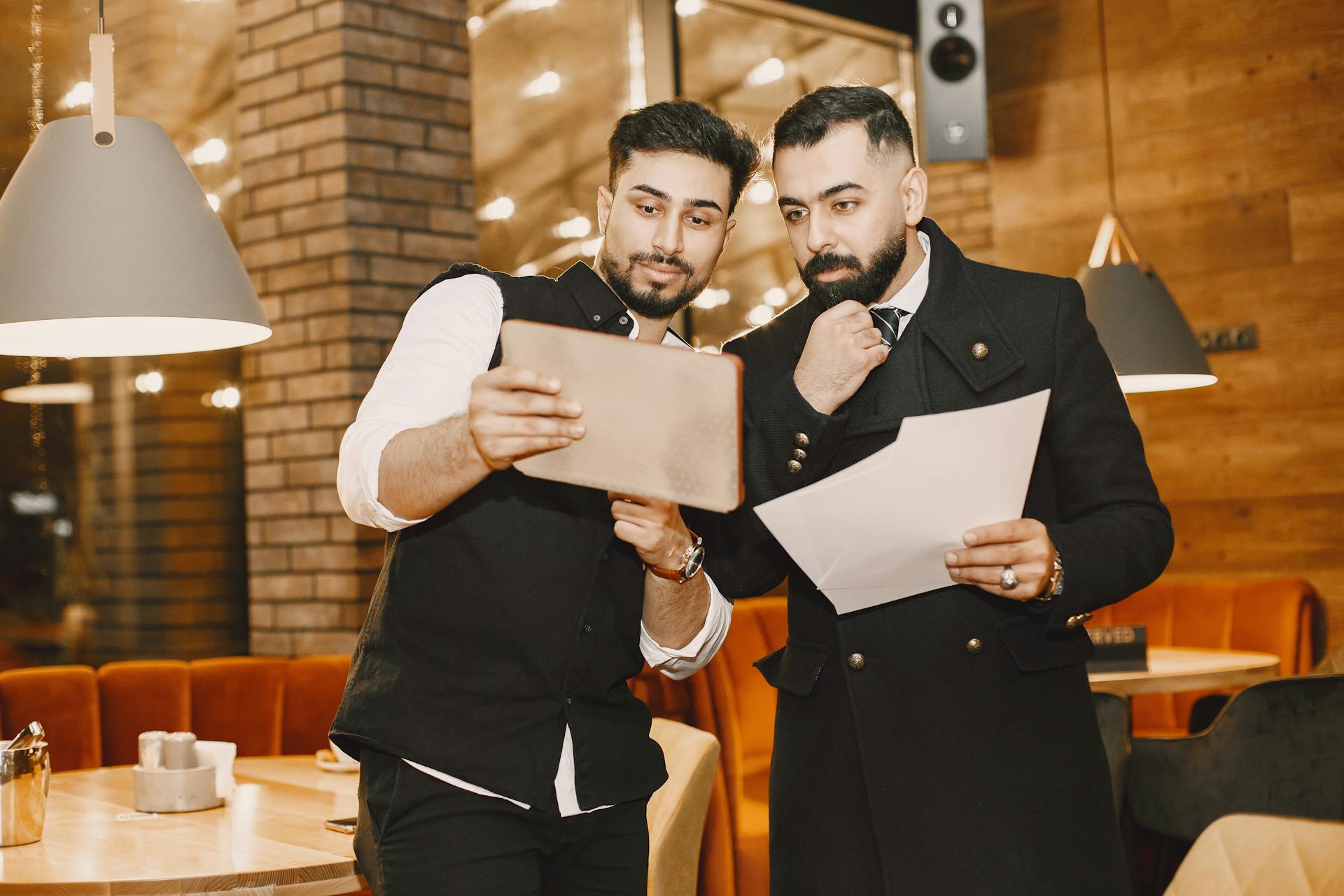 Two men in a restaurant review business documents and a tablet for planning purposes.