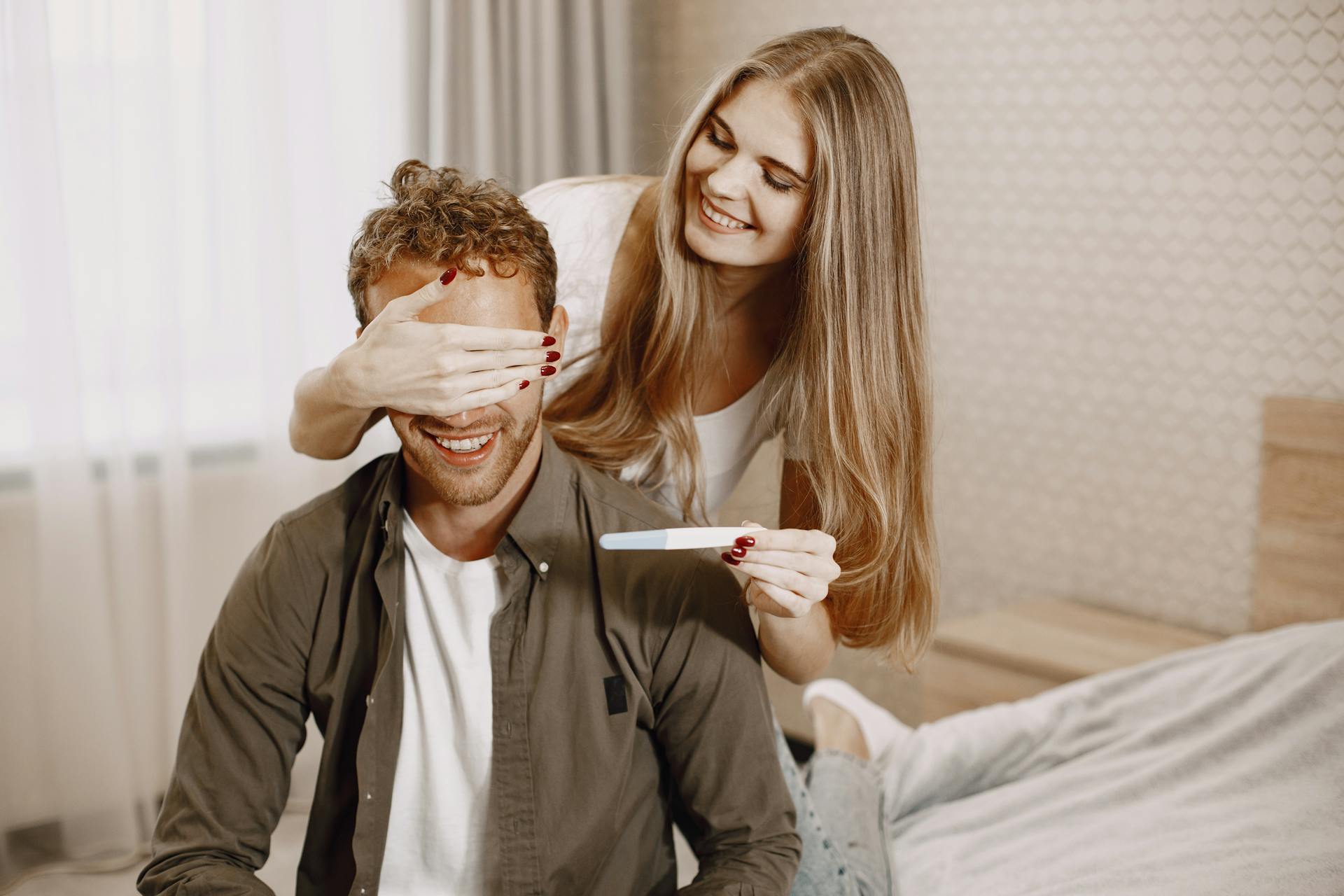 A couple joyfully celebrates a positive pregnancy test result in their cozy home.