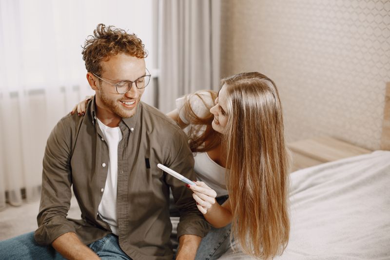 Joyful couple sitting on bed, holding a pregnancy test, embracing new beginnings.