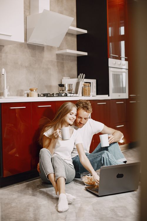 Free Happy couple enjoying morning coffee while watching a laptop in their stylish kitchen. Stock Photo