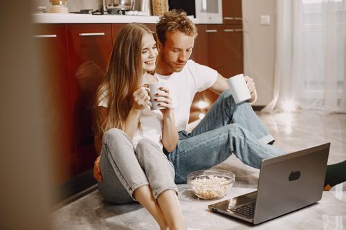 Free Young couple enjoying a cozy moment with popcorn and coffee by the computer at home. Stock Photo