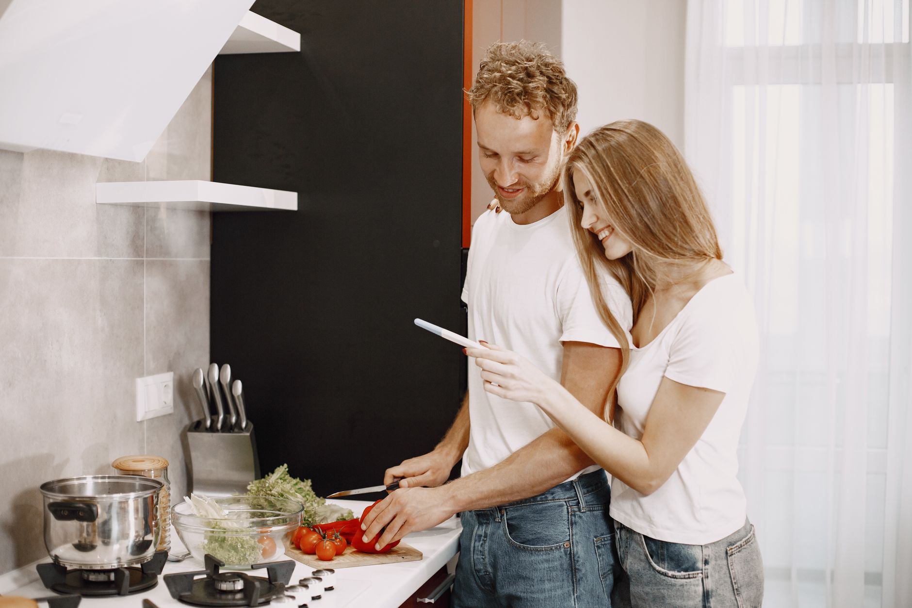 Couple happily preparing a healthy meal together in a modern kitchen setting.
