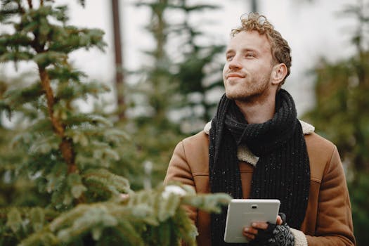 Caucasian man in winter clothing holds a tablet amidst evergreen trees, exuding a sense of tranquility.