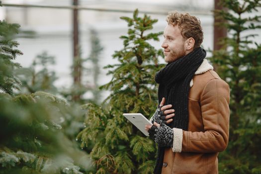Caucasian man in winter coat and scarf with a tablet in an outdoor setting.