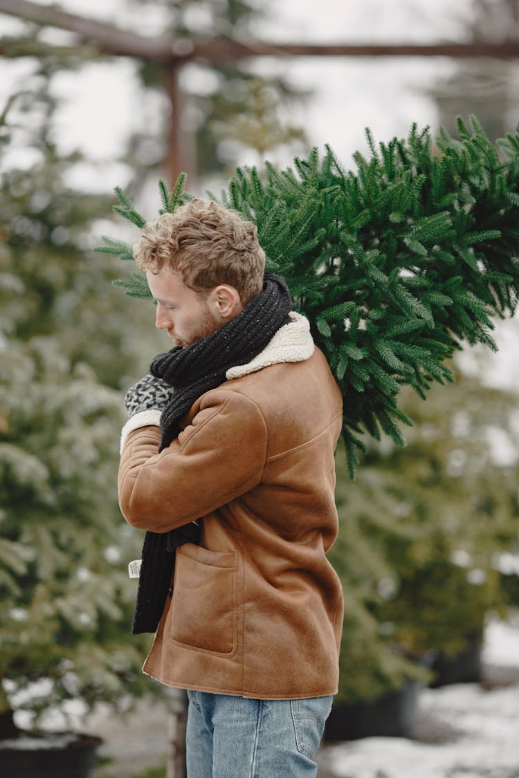 A Man In Brown Leather Jacket Carrying Christmas Tree