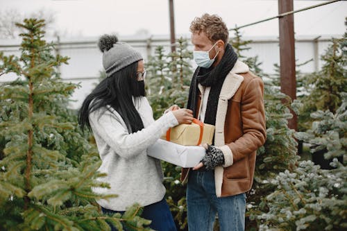 A Couple Holding Gift Boxes near the Christmas Trees