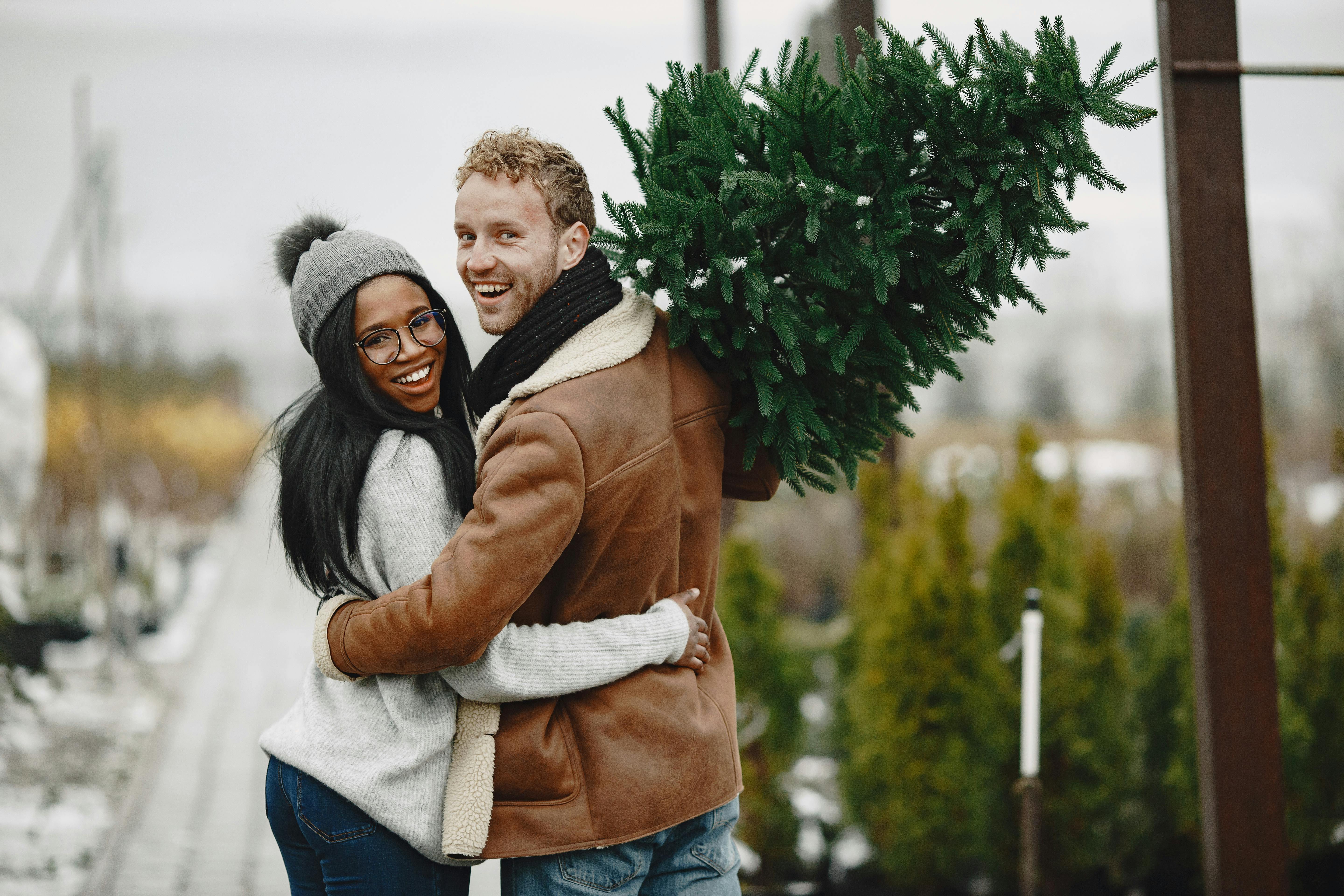 Joyful couple embracing outdoors with a festive Christmas tree, conveying warmth and holiday spirit.