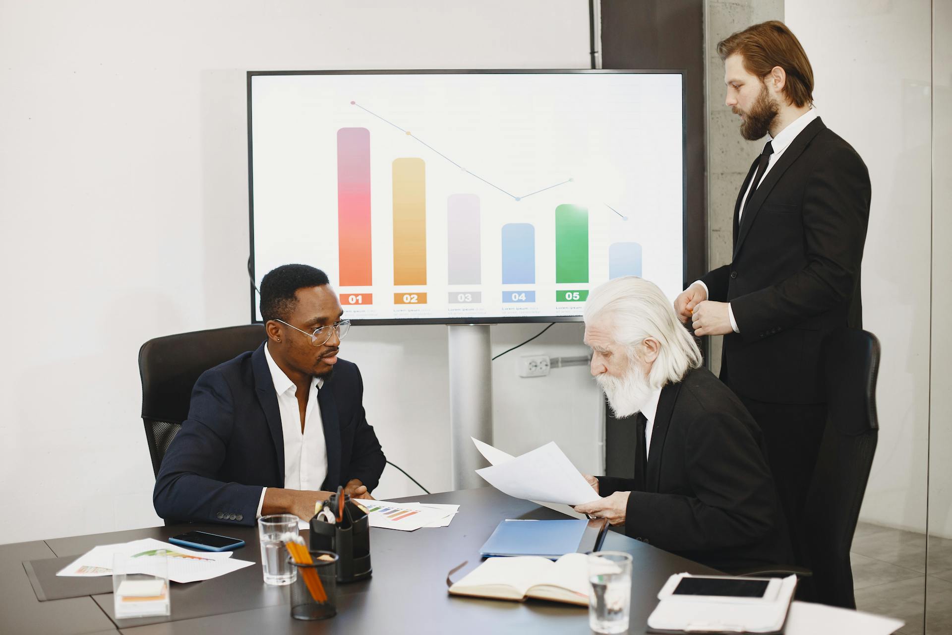 Three businessmen discussing financial data in a modern office setting with charts.