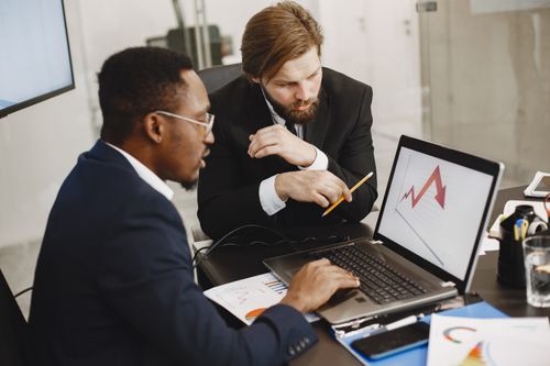 Free Two business professionals discuss marketing data on a laptop in a modern office. Stock Photo