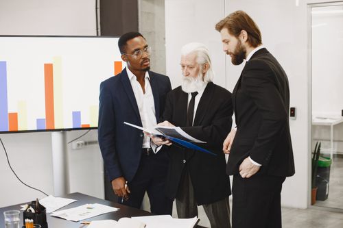 Free Three businessmen in suits discussing reports in a modern office setting. Stock Photo