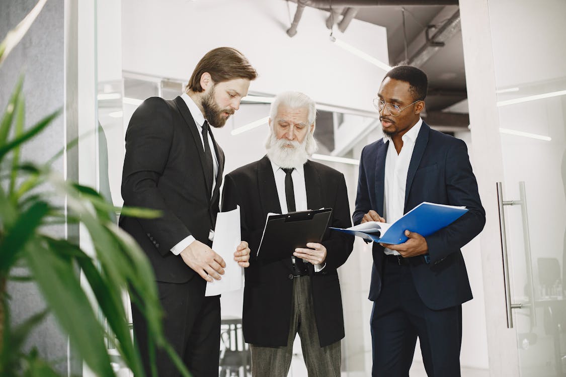 Free Diverse businessmen in professional attire discussing documents during an office meeting. Stock Photo Free Diverse businessmen in professional attire discussing documents during an office meeting. Stock Photo