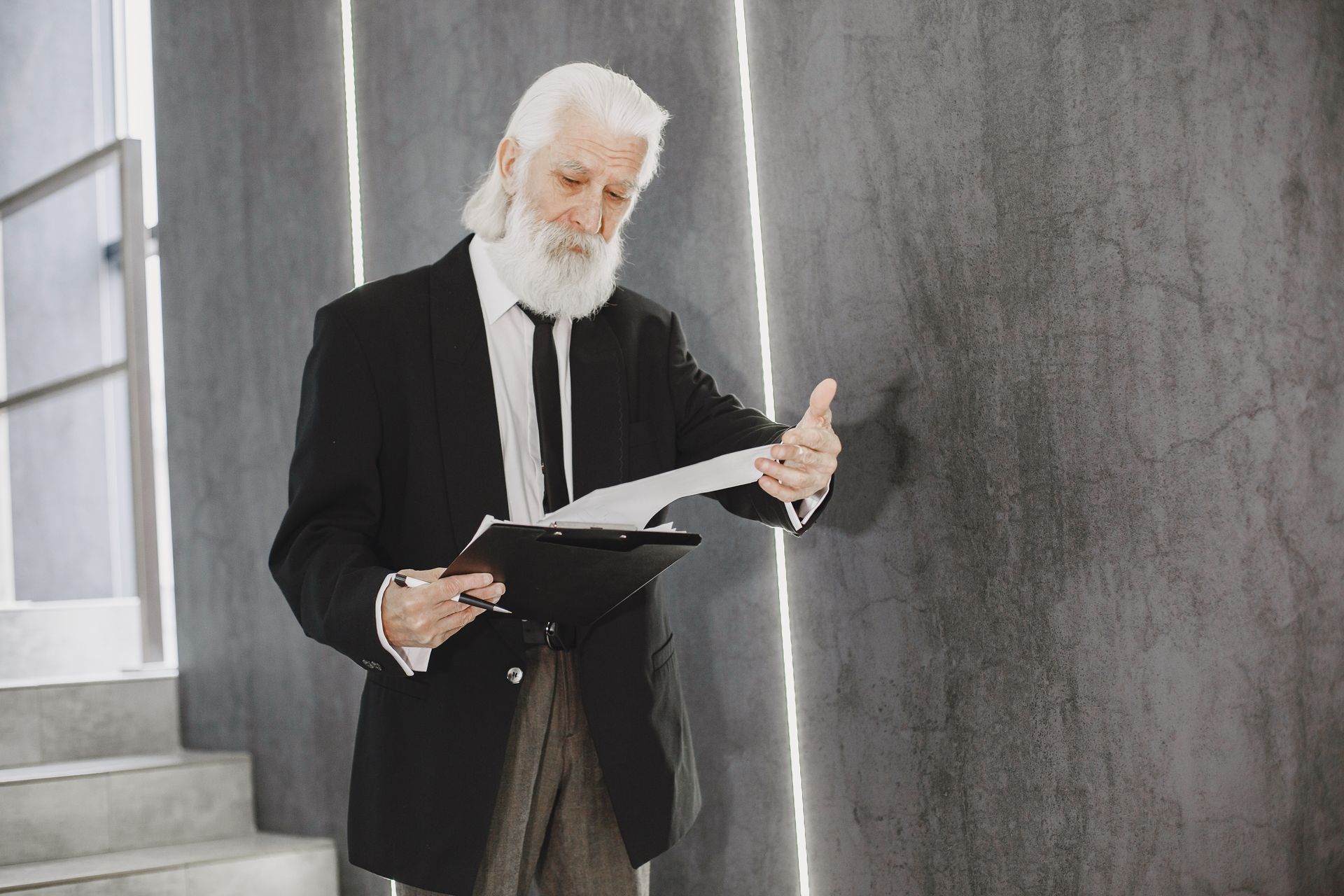 Senior man with white beard in suit reviewing documents indoors, in modern office setting.