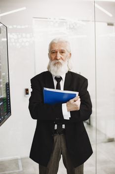 Senior businessman with beard and white hair holding documents in a modern office setting.