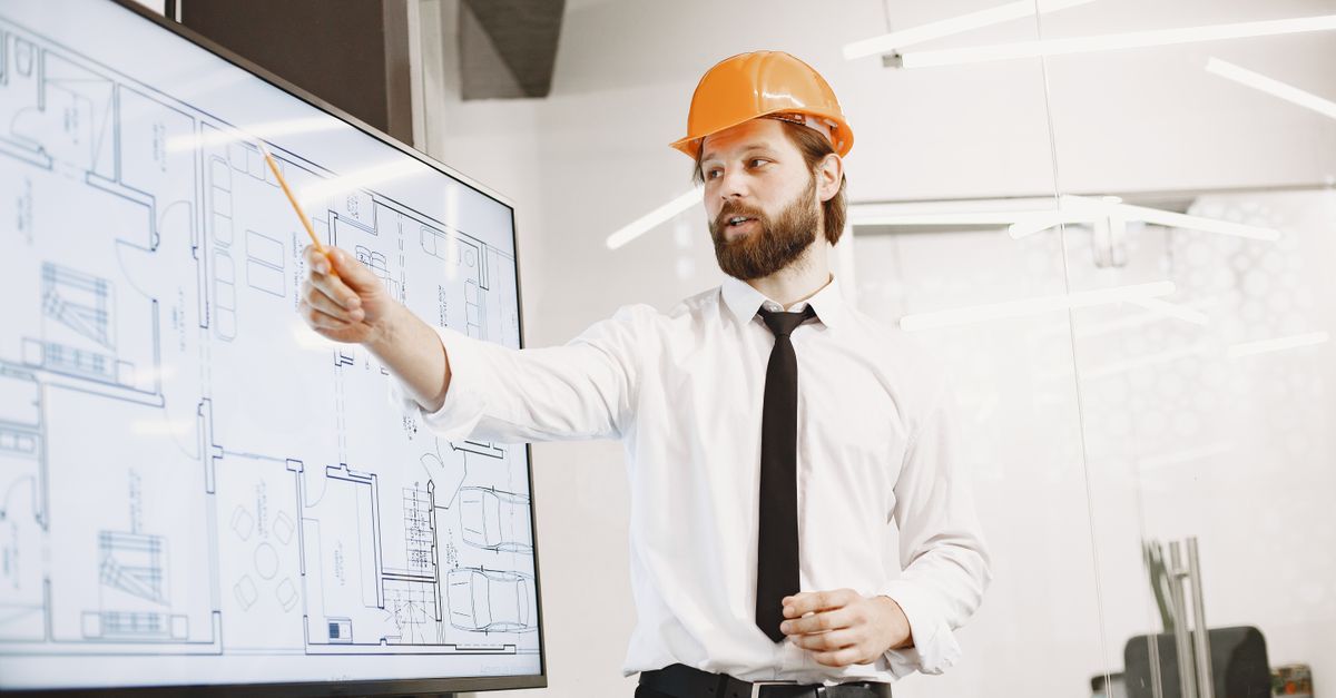 Architect with helmet presenting building blueprints on screen in modern office environment.