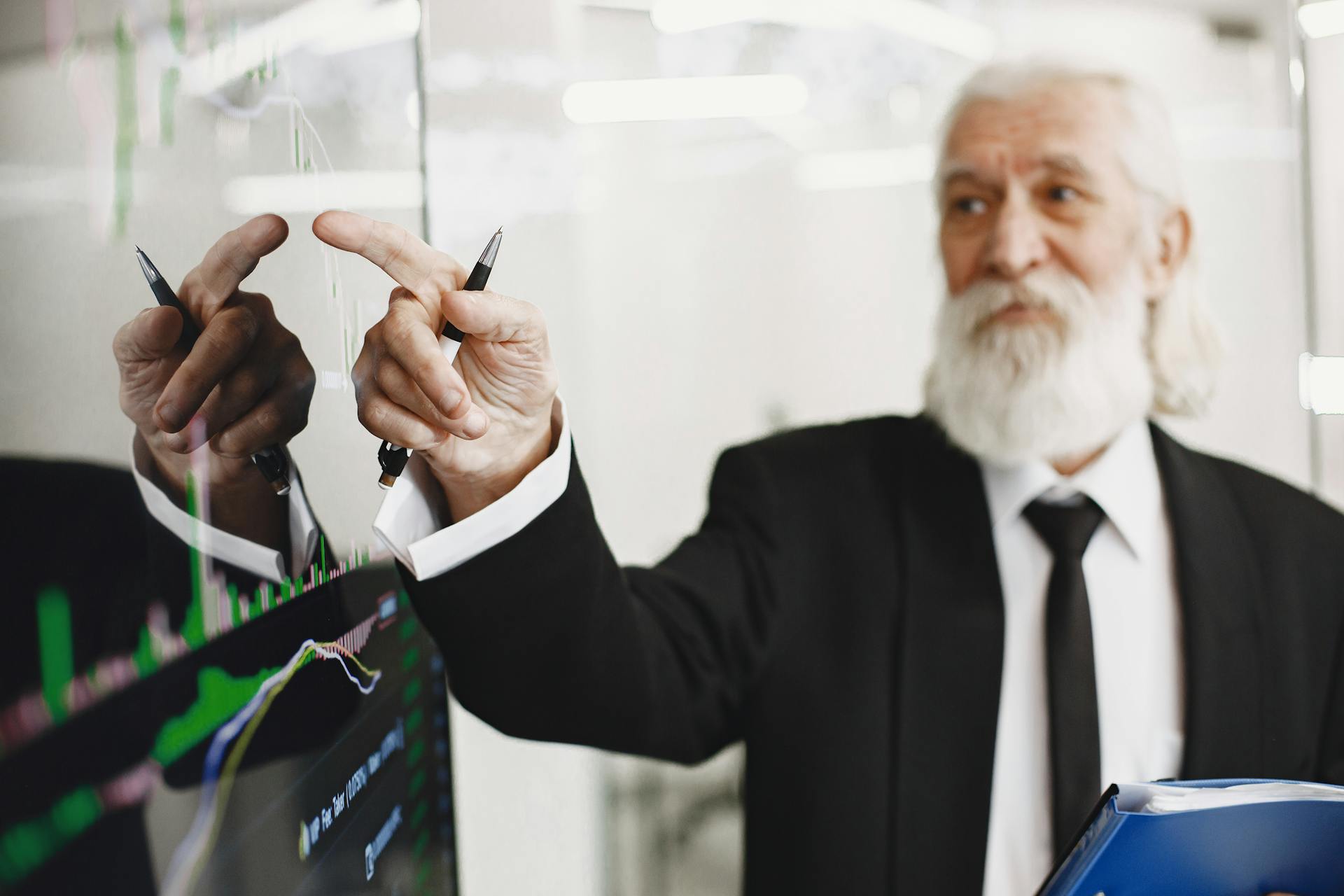 Elderly businessman with beard presenting financial trends on a screen.