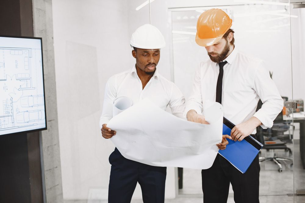 BinaCorp project manager and engineer in hard hats reviewing blueprints on site