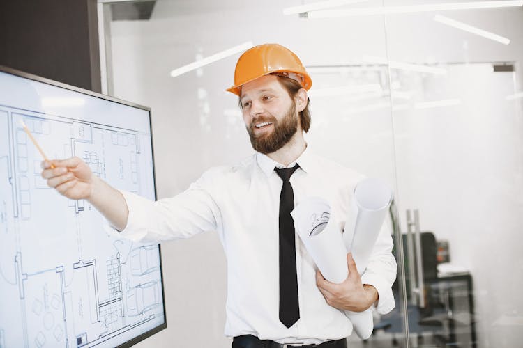 Man In A Shirt And Tie Wearing A Construction Helmet On A Meeting In An Office