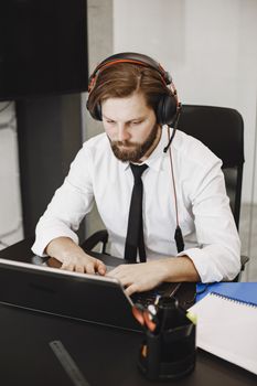 Professional man with headset working on laptop at an office desk, focused and engaged.