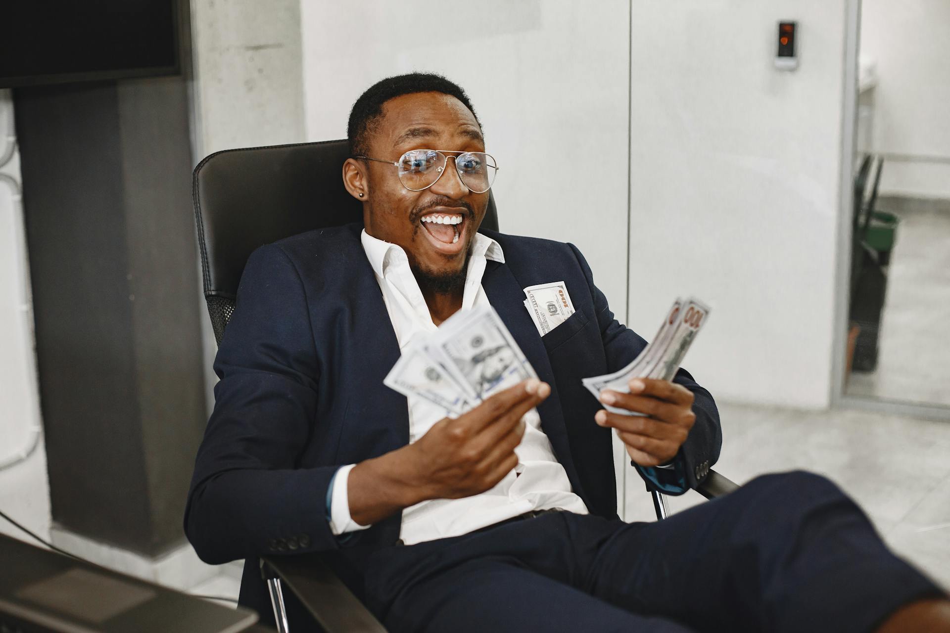 Joyful businessman in suit holding dollar bills, symbolizing success and financial achievement.