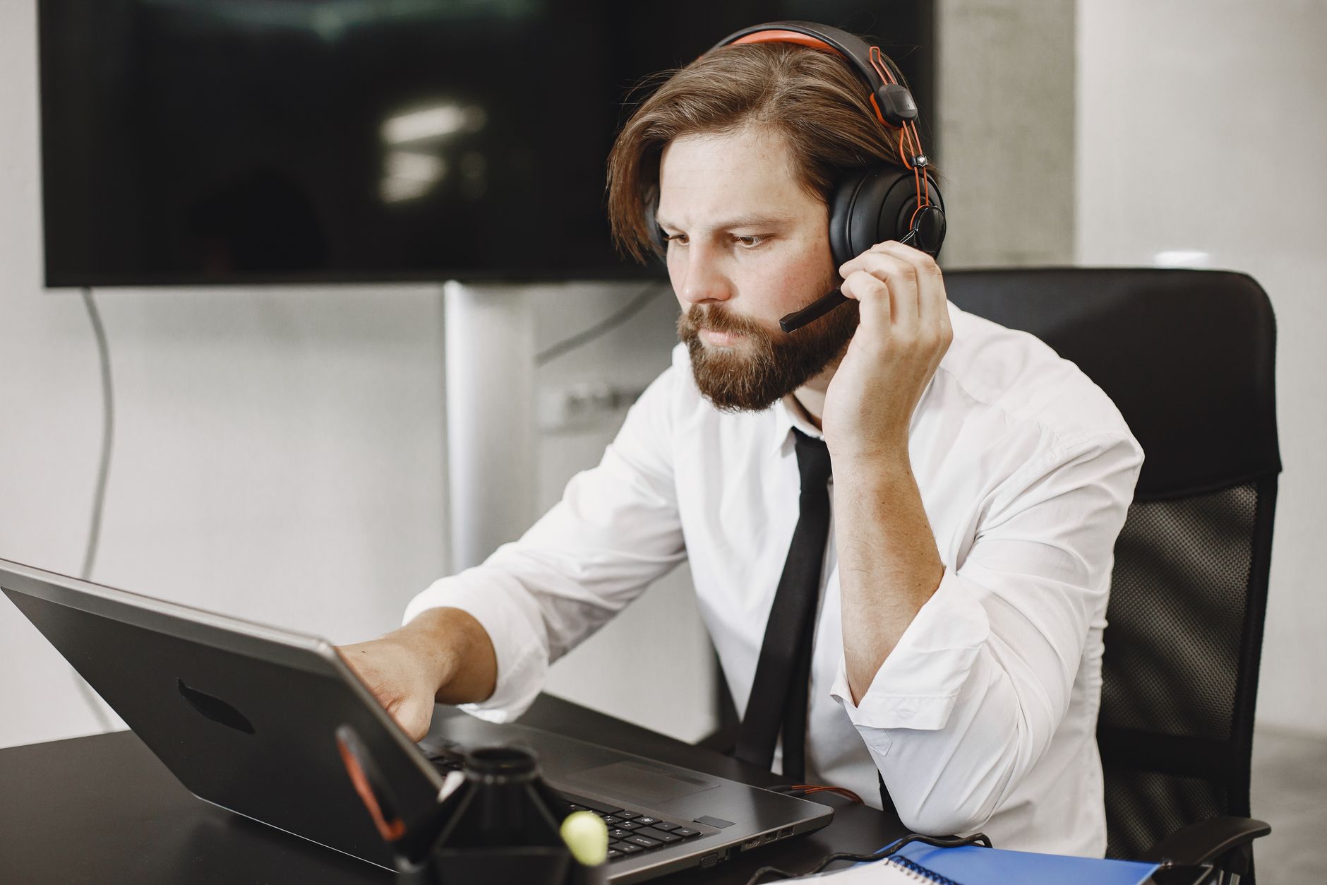 Focused man in office attire using laptop and headset, ideal for remote work themes.