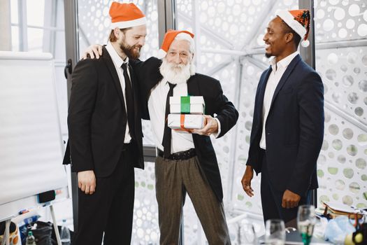 Businessmen in suits celebrating Christmas with gifts in an office setting.