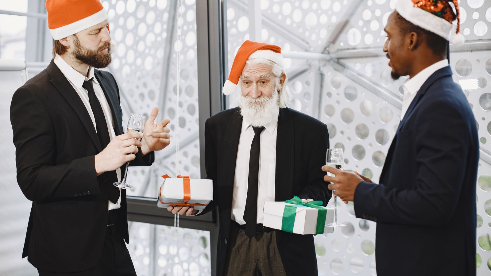 Colleagues in Santa hats trading wrapped gifts and raising a toast at an office party