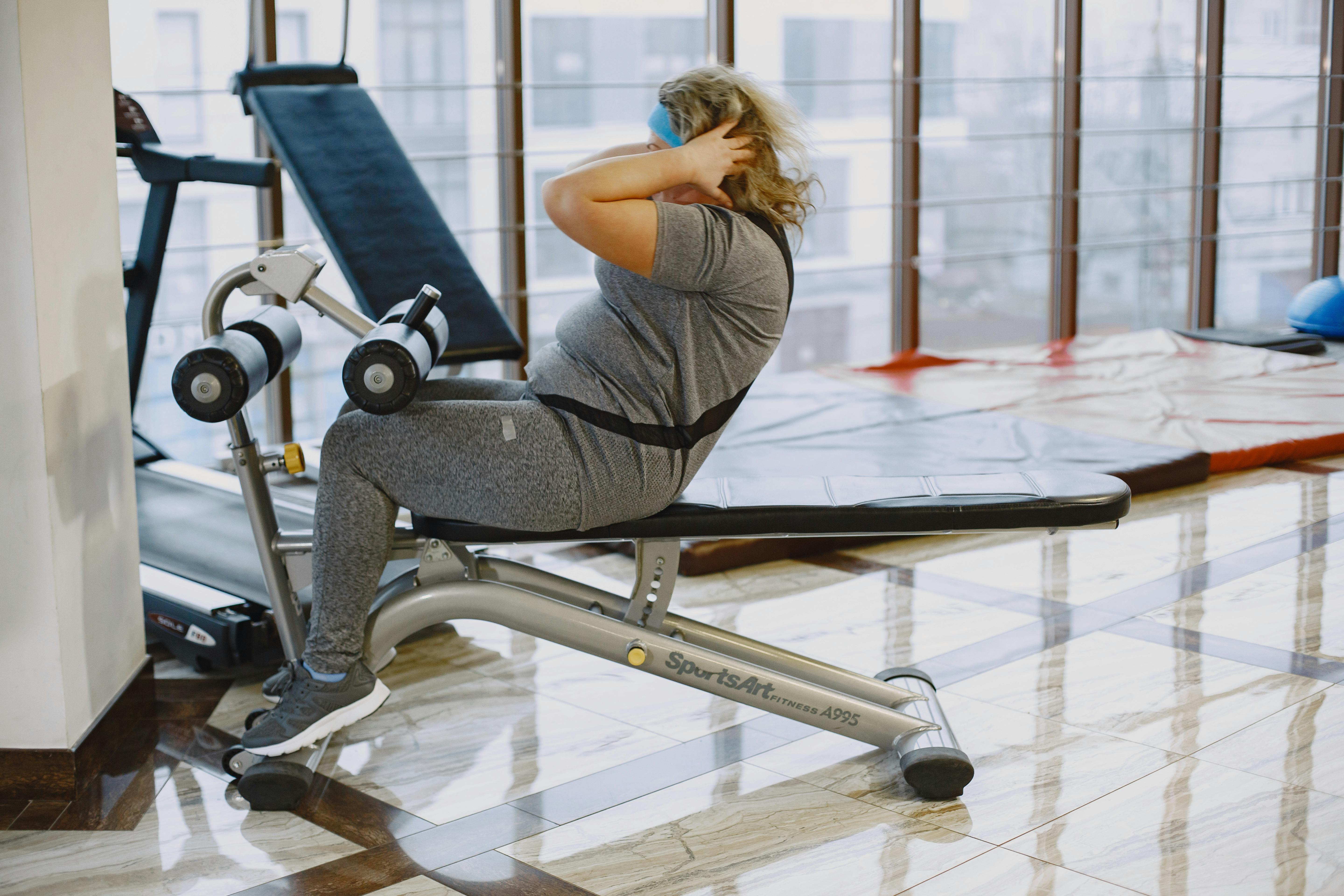 A woman performing sit-ups in a gym using a sit-up bench, focusing on fitness and exercise.