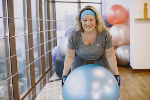 Free An adult woman engaging in a fitness workout with an exercise ball in a gym setting. Stock Photo