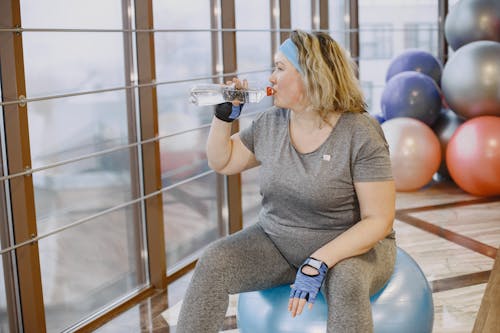 Woman Drinking Water while Sitting on a Exercise Ball