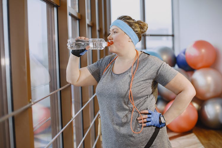 Woman Drinking Water In A Gym Room 
