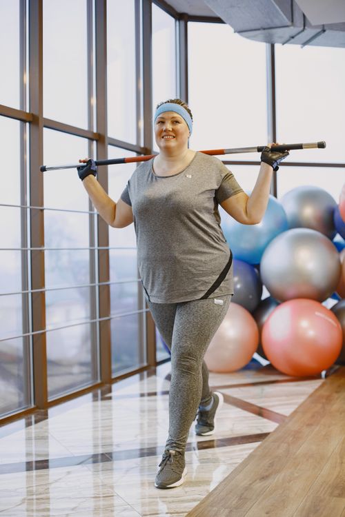 Free Woman practicing squats with a fitness stick indoors, surrounded by exercise balls. Stock Photo