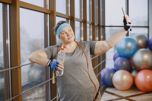 Free A smiling woman in a gym taking a selfie during her workout, showcasing a positive and active lifestyle. Stock Photo