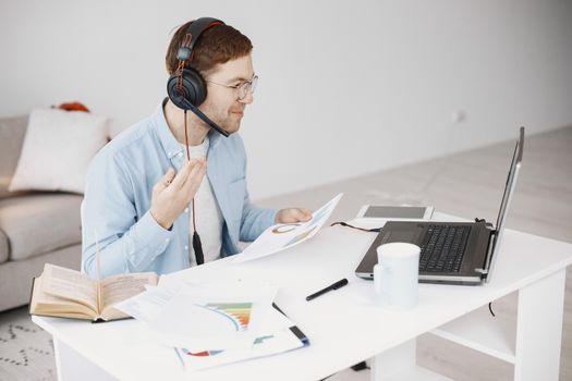 Businessman working remotely with laptop, headphones, and documents.