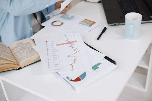 Office workspace with data charts, book, and laptop on a white desk.