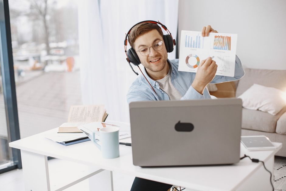 Smiling man with headphones showing graphs during a virtual meeting.