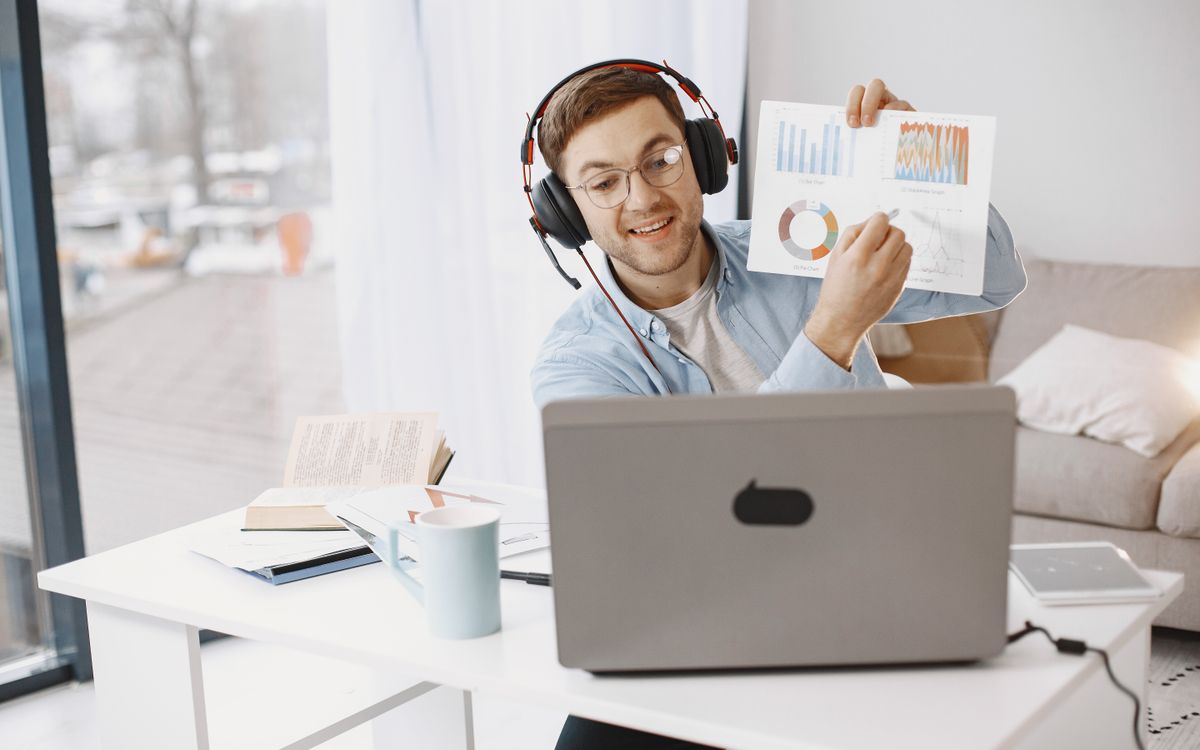 Smiling man with headphones showing graphs during a virtual meeting.