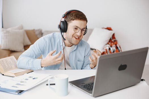 Young man wearing headphones engaged in a video call working remotely from his living room.