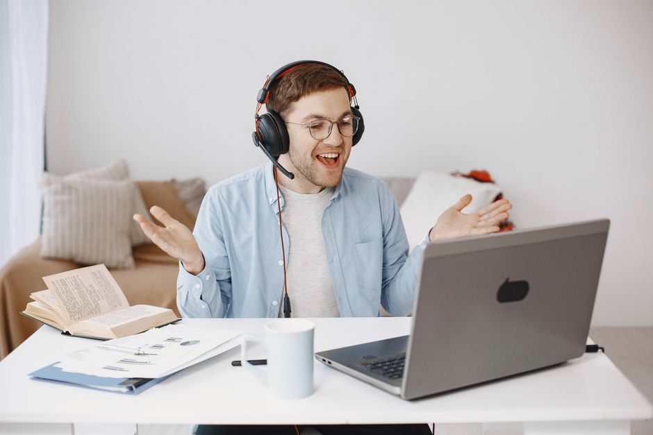 Smiling man wearing headphones having a video call on a laptop in a home office setting.