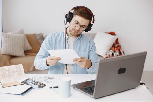 Free Adult man focused on documents while working remotely at home with laptop and headphones. Stock Photo