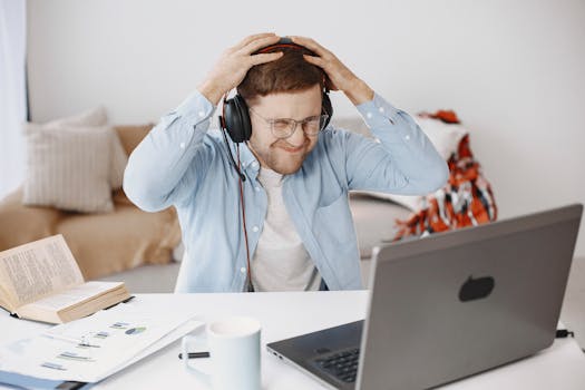 A frustrated man with headphones working at home office, laptop on desk.