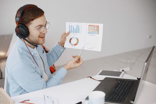 Businessman using laptop and headphones while discussing charts in a bright office setting.