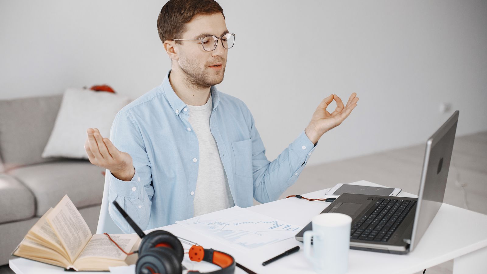 A man meditating at a desk with a laptop, books and headphones nearby
