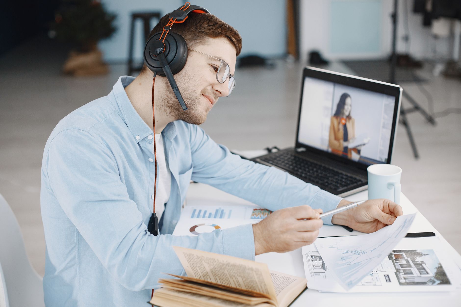 Man working remotely with headphones, reviewing documents, and video conferencing on laptop. Related image for 2025 USA Hotel Cybersecurity Briefing.