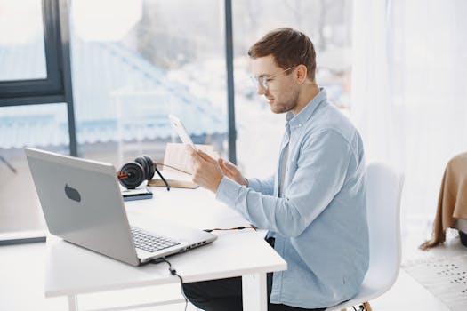 Professional man using a tablet at a modern home workspace with a laptop.
