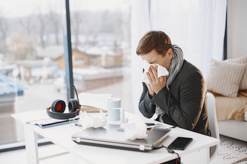 Ill Man Sitting at Desk and Sneezing 